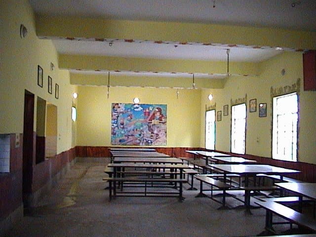 The school dining hall, with long bench tables and a mural at the end