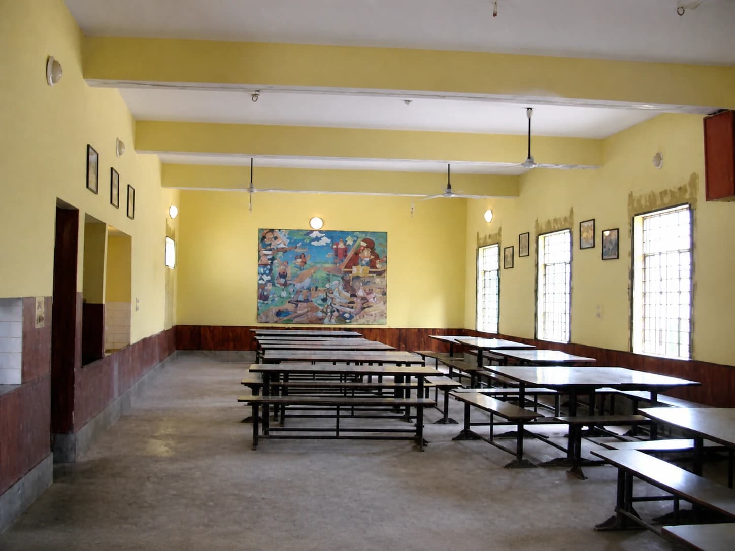 The school dining hall, with long bench tables and a mural at the end